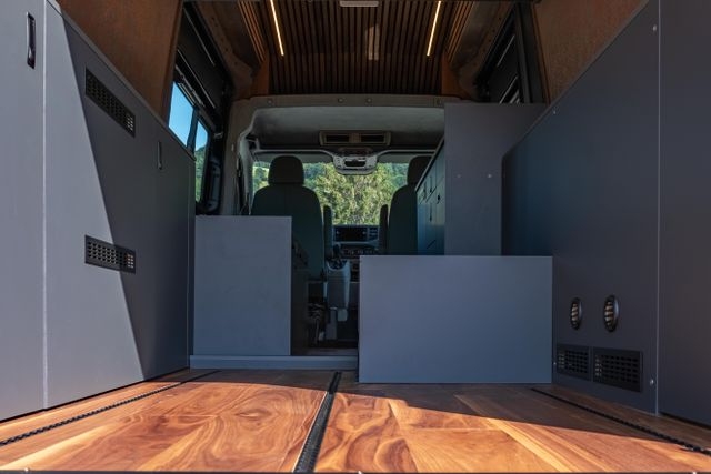 Der Boden der Garage vom Camper Van von Cocoon ist aus amerikanischem Nussbaum. In den Boden sind Airline Schienen für die Ladesicherung eingelassen. Seitlich sind graue Möbel eingebaut, in denen die ganze Technik verstaut ist.