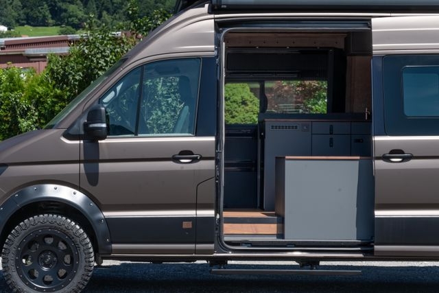Blick seitlich in den Camper Van durch die geöffnete Seitentüre. Die geöffnete Türe gibt den Blick auf individuell geschreinerte Möbel im Camper Van von Cocoon Vans frei